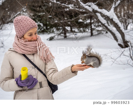 Girl feeds a squirrel with nuts at winter. Caring for animals in winter or autumn. 99603923