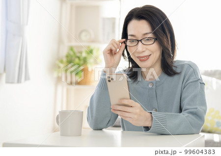 老眼鏡をかけてスマートフォンの画面を見るアラフィフの女性 老眼鏡をかけてスマートフォンの画面を見るアラフィフの女性 99604383