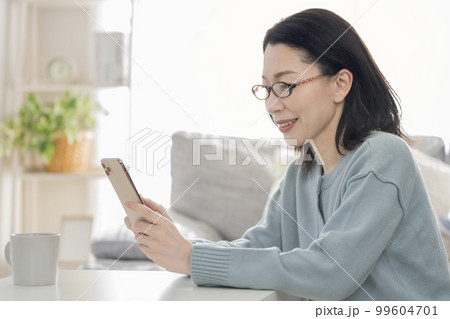 老眼鏡をかけてスマートフォンを操作するアラフィフの女性 99604701