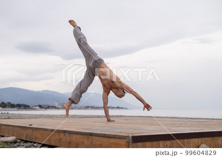 Shirtless caucasian man doing acrobatic wheel on the beach.  99604829