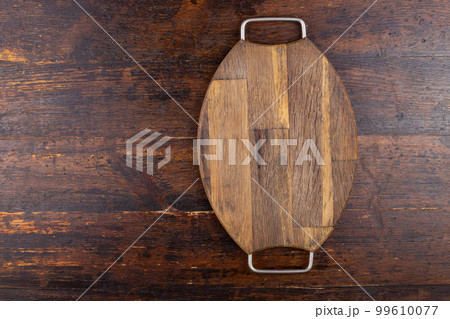 Wooden cutting board with iron handles on a wooden background. View from above 99610077