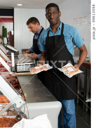 Two butchers arranging meat display 99613098