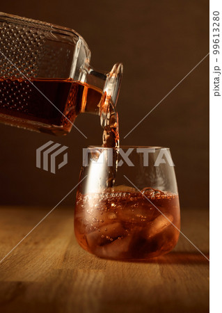 Whiskey is poured into a dammed glass with ice. 99613280
