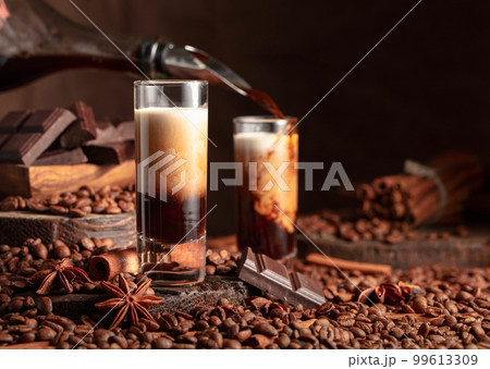Irish cream and coffee liquor is poured from a bottle into a glass. Irish cream and coffee liquor is poured from a bottle into a glass. 99613309