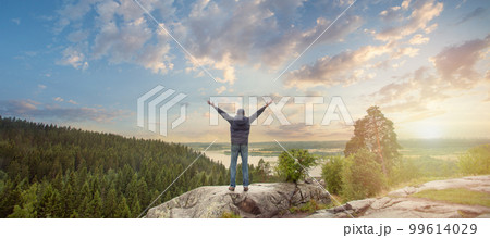 Man looking at the beautiful view of sunrise with arms outstretched on mountain top Man looking at the beautiful view of sunrise with arms outstretched on mountain top 99614029
