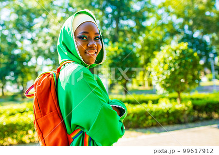 african woman in green hijab with bright makeup with rainbow backpack in summer park african woman in green hijab with bright makeup with rainbow backpack in summer park 99617912