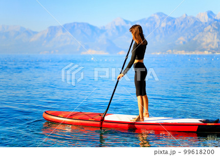 Woman standing on sup board and enjoying peace and quiet outdoors 99618200