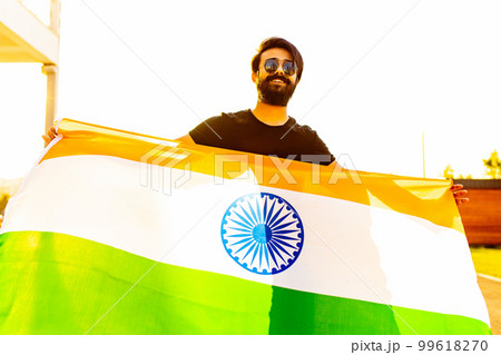 handsome indian bearded man in black cotton t-shirt wawing indian flag in summer park at sunset golg light handsome indian bearded man in black cotton t-shirt wawing indian flag in summer park at sunset golg light 99618270