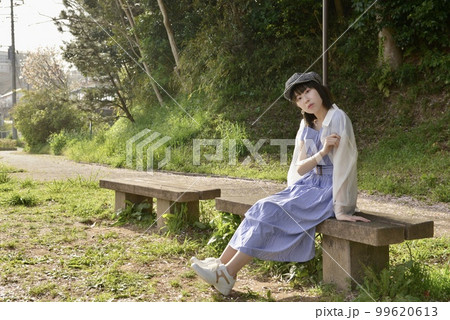 公園のベンチに座りポーズをとるワンピース姿の若い女性 公園のベンチに座りポーズをとるワンピース姿の若い女性 99620613