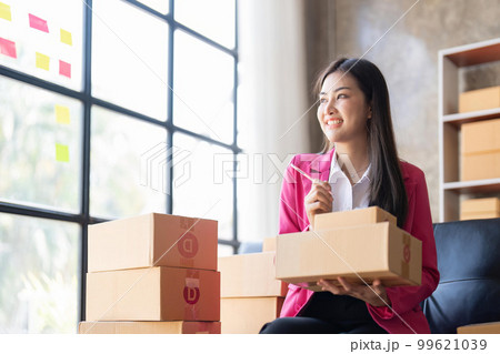 Young woman, an Asian online business owner, smiles, prepares parcel boxes and checks online orders for products to be delivered to customers 99621039