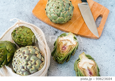 Sliced artichoke and kitchen knife on on wooden cutting board on table. Healthy food vegetables. 99623684