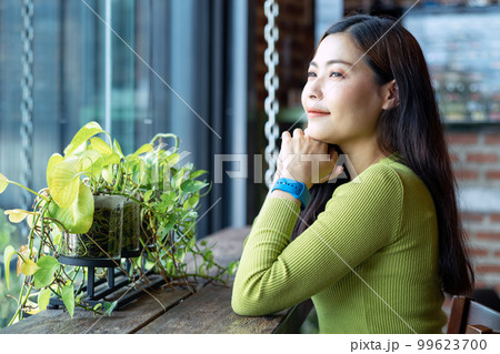 Asian beautiful young woman in green sweater sitting near cafe window and looking outside Asian beautiful young woman in green sweater sitting near cafe window and looking outside 99623700