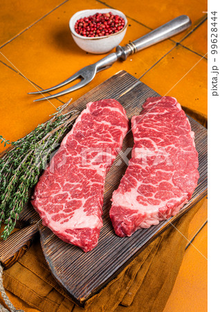 Raw Denver beef meat Steak with pink pepper and thyme. Orange background. Top view Raw Denver beef meat Steak with pink pepper and thyme. Orange background. Top view 99628444