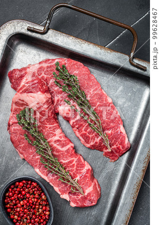 Uncooked Raw Denver beef meat Steak with pink pepper and thyme on a steel tray. Black background. Top view Uncooked Raw Denver beef meat Steak with pink pepper and thyme on a steel tray. Black background. Top view 99628467