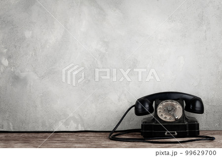 Retro black rotary telephone on wooden table in front gray concrete background Retro black rotary telephone on wooden table in front gray concrete background 99629700