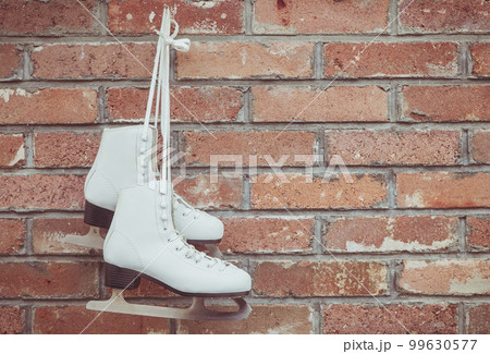 White figure skating skates hang on a brick wall in a barn White figure skating skates hang on a brick wall in a barn 99630577