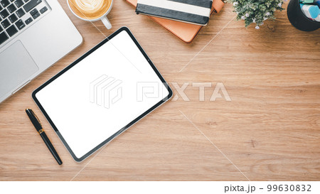 Wooden desk workplace with blank screen tablet, laptop, pen, notebook and cup of coffee, Top view flat lay with copy space. 99630832