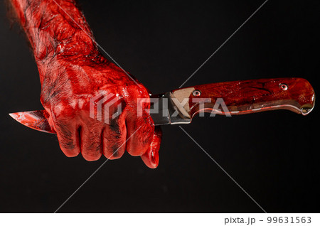 A man with bloodied hands holds a knife by the blade on a black background. A man with bloodied hands holds a knife by the blade on a black background. 99631563