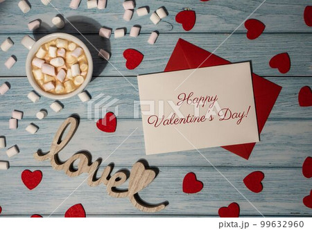 HAPPY VALENTINES DAY text Greeting card with red envelope with white cup of coffee and marshmallows on wooden background. Romantic Small hearts Valentine day. Holiday morning 99632960
