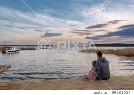 Father and daughter on the shore of the lake watching the sunse 99633957