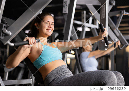Young woman trains her arm muscles using a simulator in gym 99636229