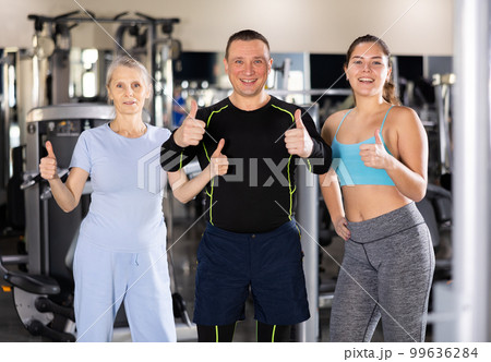 Two sportswomen and one sportsman standing in middle of gym showing thumbs up Two sportswomen and one sportsman standing in middle of gym showing thumbs up 99636284