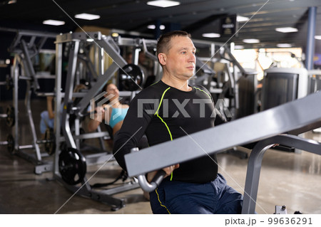 Focused sportsman working out arm muscles on the simulator in gym 99636291