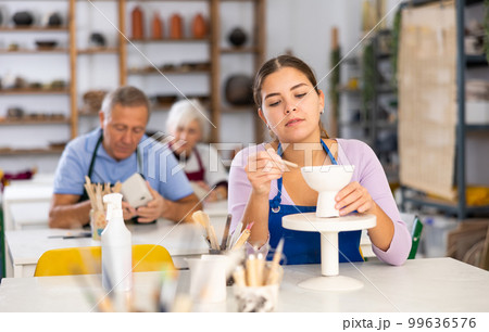Woman using spatula and a knife creates dishes from soft clay 99636576