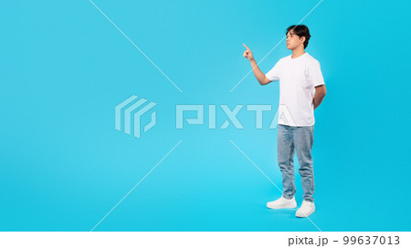 Serious Asian Teen Guy Pointing Finger Aside Over Blue Background 99637013