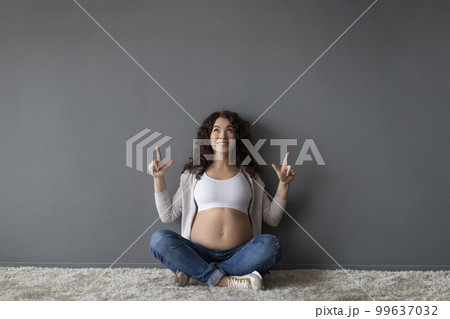 Happy Pregnant Woman Sitting On Floor And Ponting Up At Copy Space 99637032