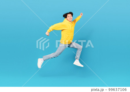 Japanese Teen Boy Jumping In Mid Air Over Blue Background Japanese Teen Boy Jumping In Mid Air Over Blue Background 99637106