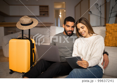 Smiling young arab male, european lady use tablet and laptop to choose country for vacation travel, buy tickets 99637241