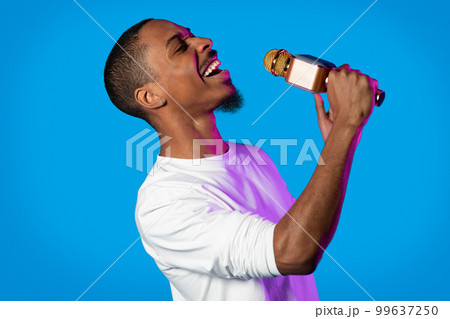 Talented young black guy singing on blue, holding microphone Talented young black guy singing on blue, holding microphone 99637250