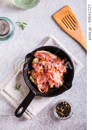 Crispy strips of bacon fried in a pan on the table. Top and vertical view 99641727