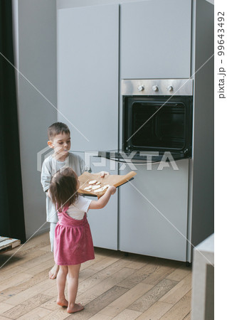 Brother helps his sister put a baking sheet in the oven. Brother helps his sister put a baking sheet in the oven. 99643492