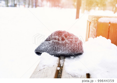 a man's hat is forgotten on a park bench in winter 99644359