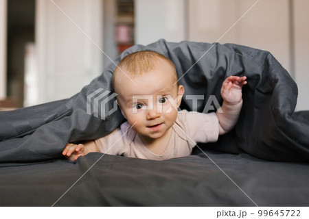 Cute baby is lying on his tummy, leaning on his wrists under the blanket 99645722