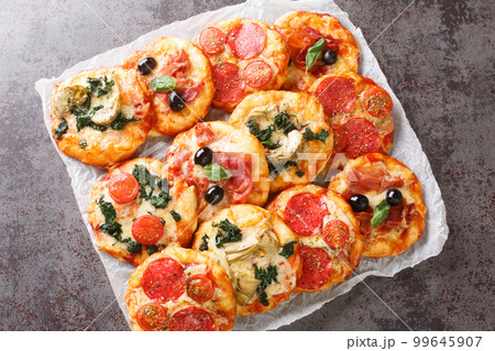 Pizzette Italian mini pizzas or pizza bites close-up on parchment. Horizontal top view Pizzette Italian mini pizzas or pizza bites close-up on parchment. Horizontal top view 99645907