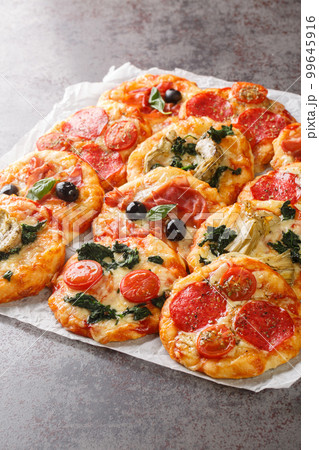 Homemade Mini Pizzas Pizzette with meaty and vegetarian toppings close-up on parchment. Vertical 99645916