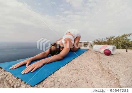 Woman sea pilates. Sporty happy middle aged woman practicing fitness on beach near sea, smiling active female training on yoga mat outside, enjoying healthy lifestyle, harmony and meditation. 99647281