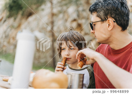 Close-up view of father hugs his school boy son on a family picnic in the mountains. Child kid and his dad taking a rest and enjoying a picnic while hiking in the mountains 99648899