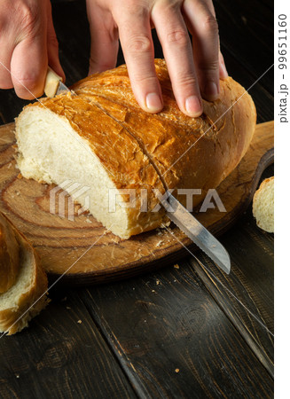 The chef cuts fresh bread with a knife on a kitchen cutting board for lunch. Healthy food and traditional bakery concept The chef cuts fresh bread with a knife on a kitchen cutting board for lunch. Healthy food and traditional bakery concept 99651160