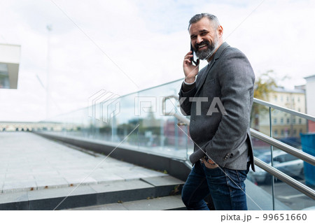 mature adult businessman talking on the phone turning around looking smiling at the camera 99651660