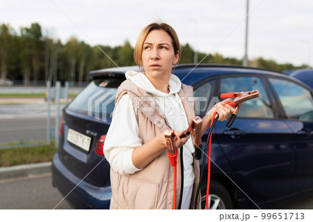 adult woman stands car installer with wires to charge battery adult woman stands car installer with wires to charge battery 99651713