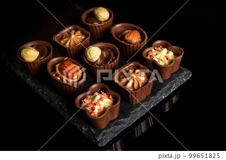 Candy with cream and nuts on a slate board. Assorted chocolate on black isolated background. Idea for dessert in a restaurant Candy with cream and nuts on a slate board. Assorted chocolate on black isolated background. Idea for dessert in a restaurant 99651825