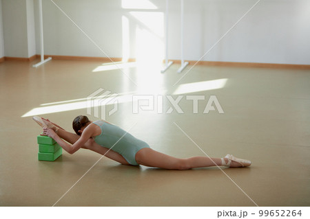 Teen girl, ballet dancer training at ballet dance school indoors on daytime. Doing stretching, sitting on twine on yoga blocks. Concept of classical ballet, art, choreography 99652264