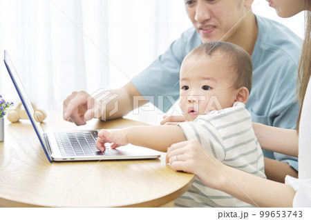 家で赤ちゃんとパソコンを見る両親 家で赤ちゃんとパソコンを見る両親 99653743