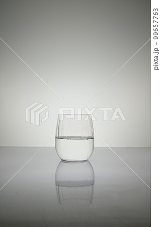 Vertical shot of water glass isolated on a white shiny surface 99657763