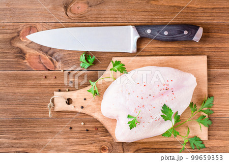 Raw chicken breast on a frame in spices and herbs on a cutting board and kitchen knife on a wooden table. Top view 99659353