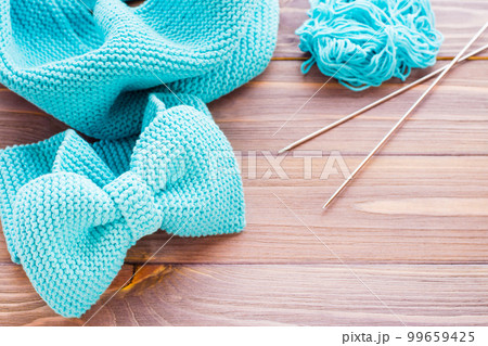 Knitted mint headband, snud, needles and  tangle on a wooden table 99659425